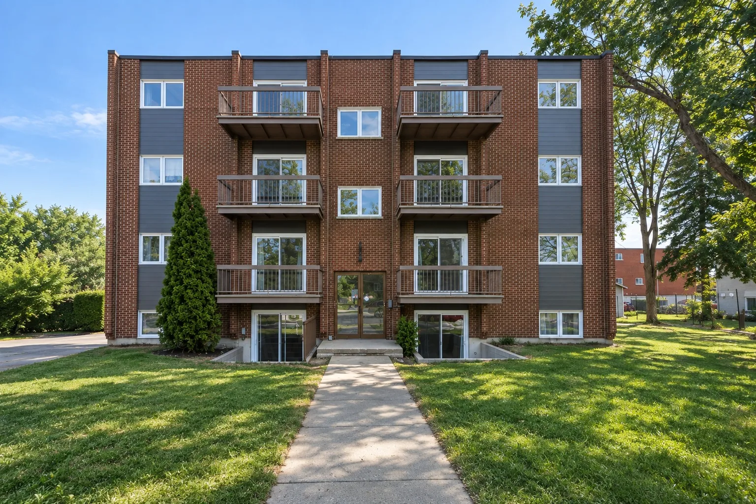 L’immeuble vu depuis la rue Roy : brique rouge, balcons et allée bordée de pelouse